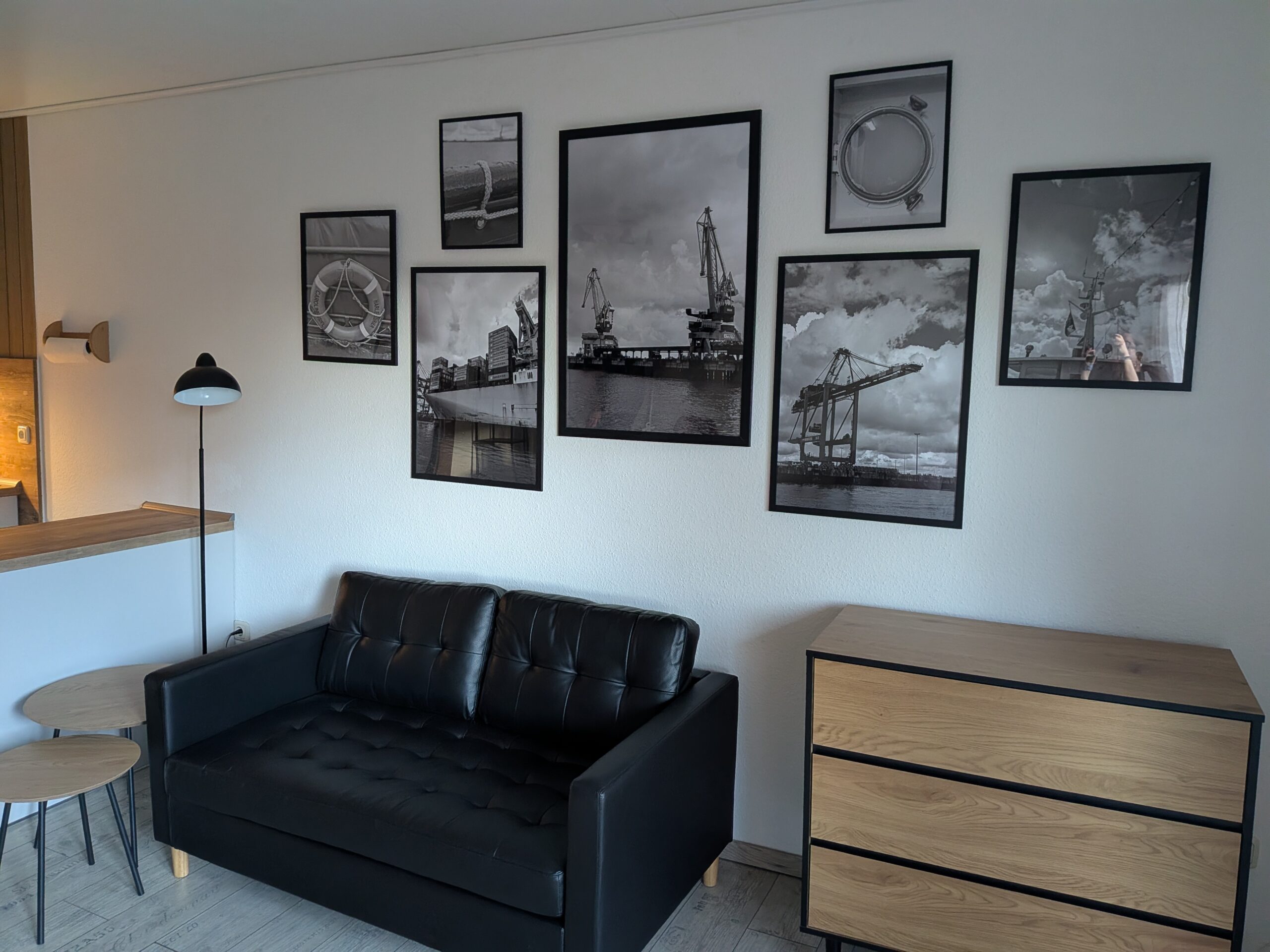 Wohnbereich mit schwarzem Sofa, Kommode und maritimer Bilderwand